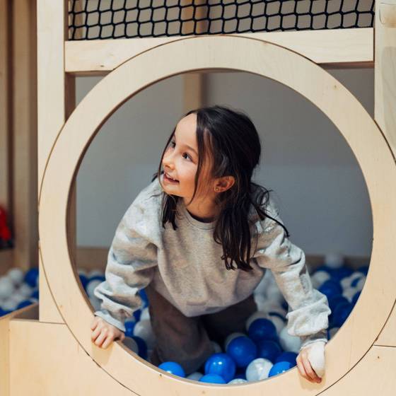 Kind im Spielzimmer von harrry's home Graz schaut durch ein rundes Holzfenster