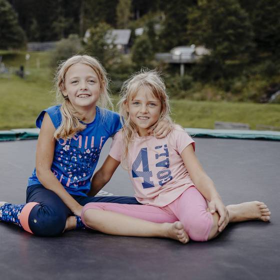 2 Mädchen sitzen am Trampolin und schauen in die Kamera. 2 Mädchen sitzen am Trampolin und schauen in die Kamera.