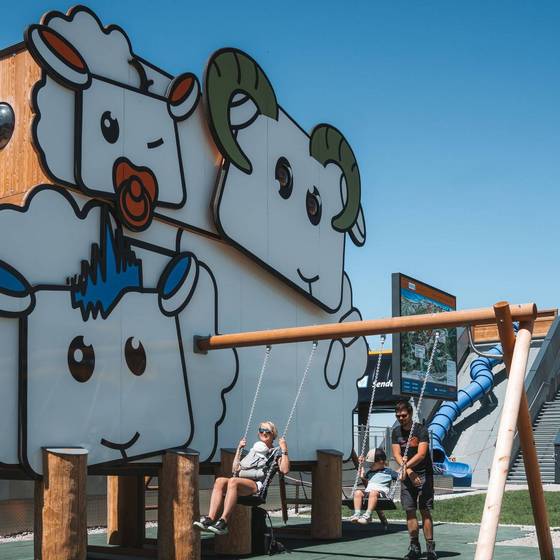 2 Kinder auf der Schaukel neben dem Spielturm mit "Fassade" aus Schafen. 2 Kinder auf der Schaukel neben dem Spielturm mit "Fassade" aus Schafen.