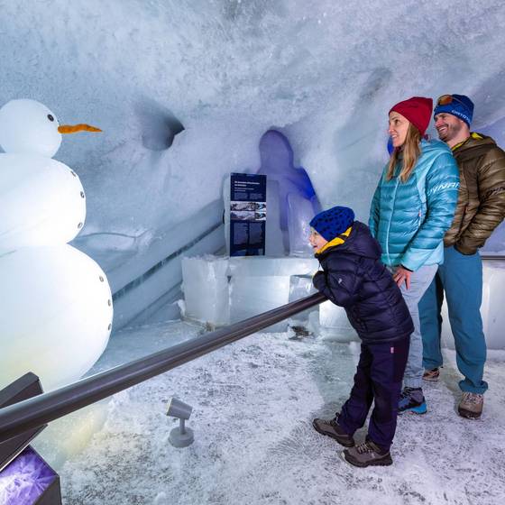Vater, Mutter und Kind betrachten einen Schneemann im Eispalast am Dachstein.