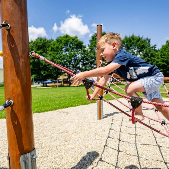 Kind/kleiner Bub klettert über ein Netz am Klettergerüst.
