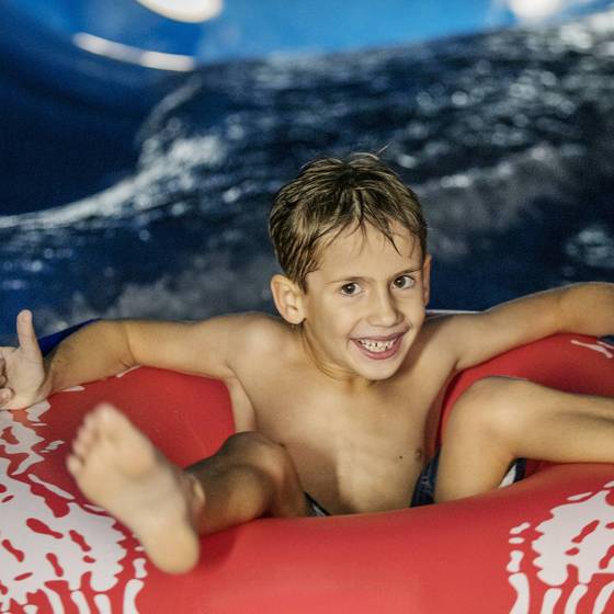 Bub sitzend in Badekleidung in einem roten Schwimmmreifen, lacht in die Kamera