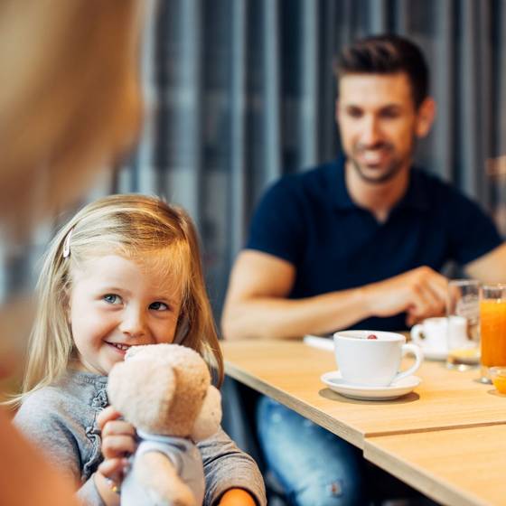 Mutter, Kind und Vater beim Frühstück im Hotel, Kind spielt mit Puppe